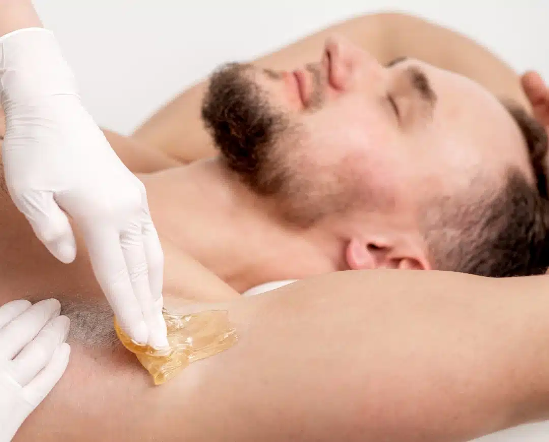 cosmetologist applying wax paste male armpit